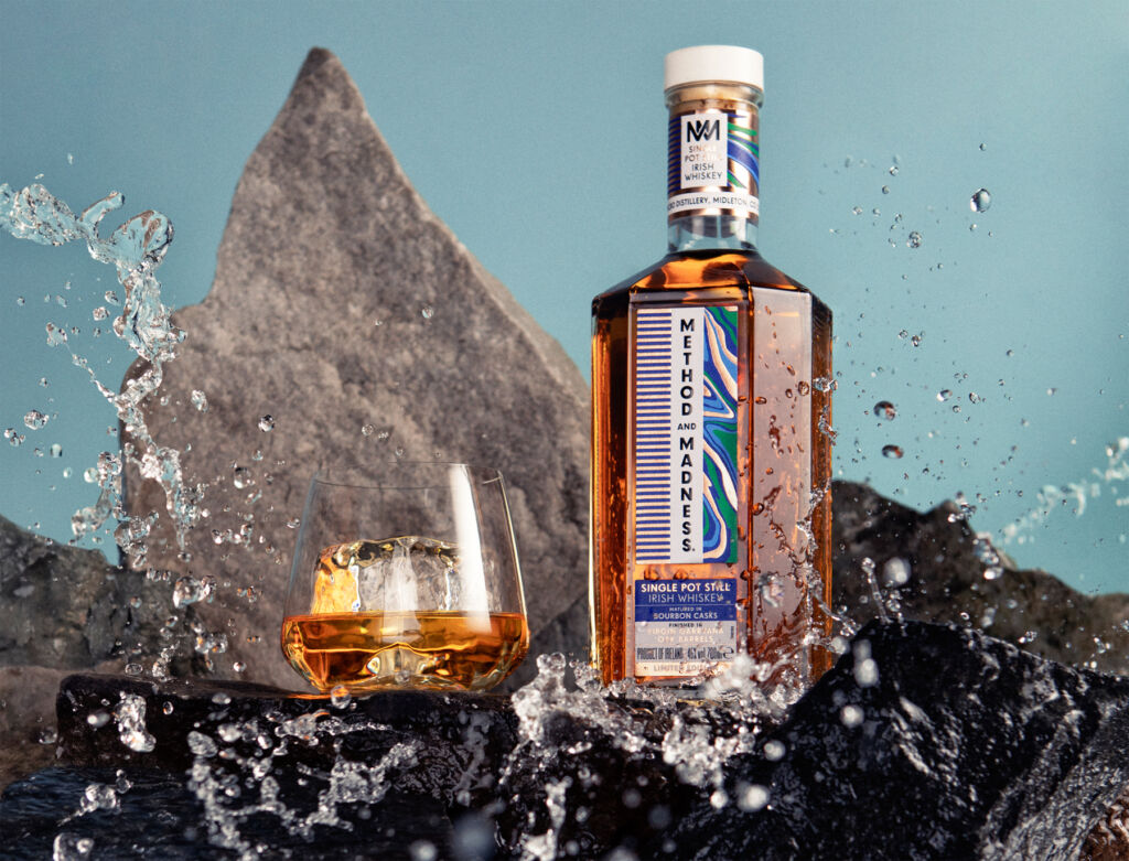 A bottle of the whisky on rocks being splashed by the seas waves