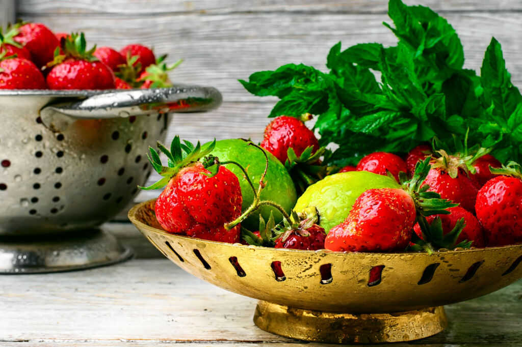A brass coloured metal bowl full of fresh strawberries