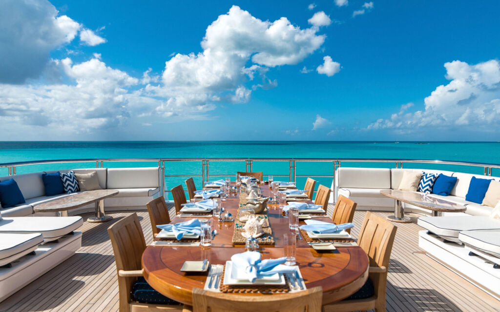 A beautiful wooden dining table on the rear of a superyacht moored in calm turquoise seas