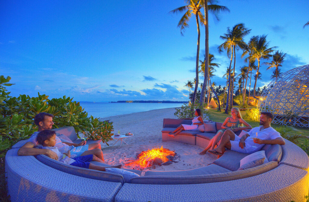 Guests relaxing by a fire on the beach in the evening