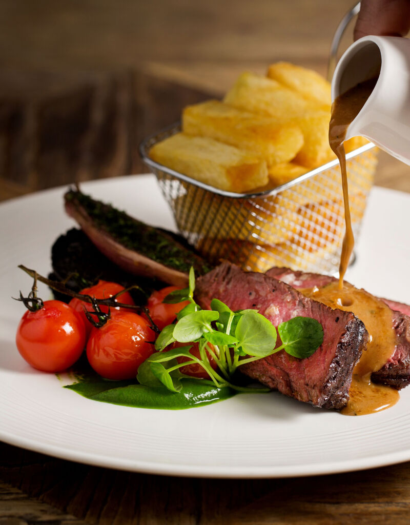 A sliced beef dish with baby tomatoes and fresh cut chips