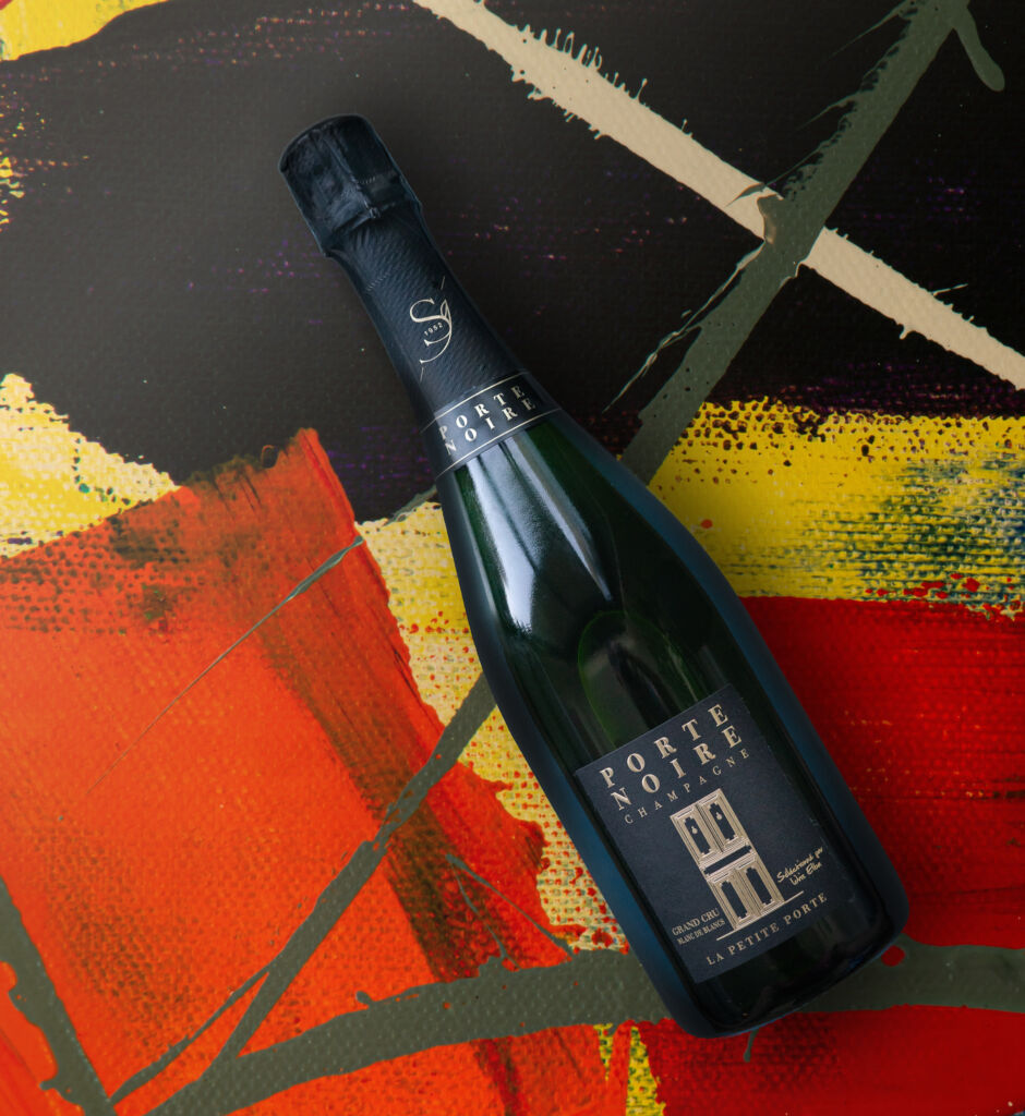 A bottle of Porte Noire champagne laying on a multi-coloured painted canvas