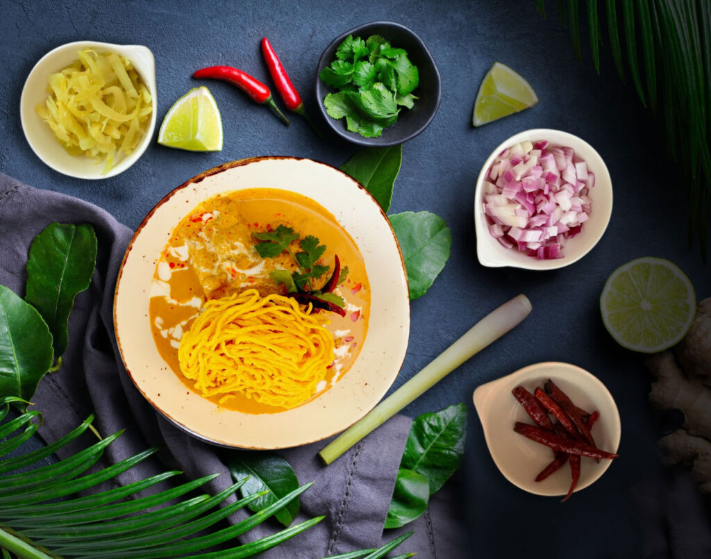 Northern Thai-Style “Khao Soi” Curry on a table with leaves and fruits