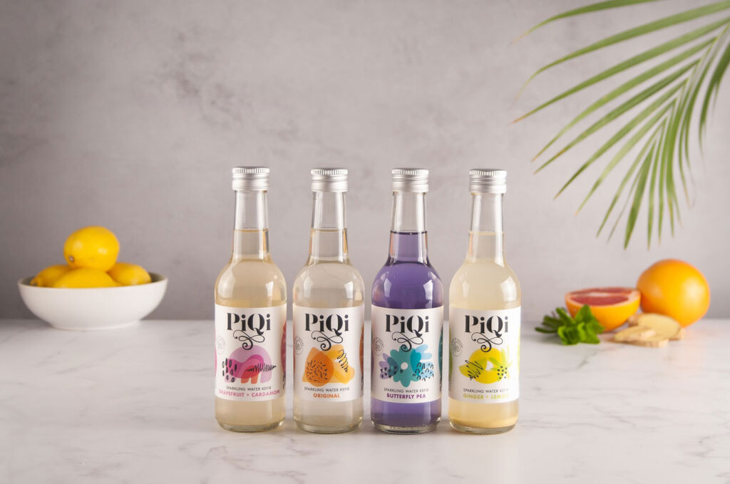 Four bottles of PiQi on a kitchen work surface with fruit in the background