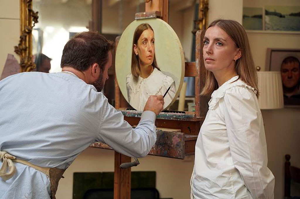 A photograph of Jamie Routley painting a portrait of a woman in his studio