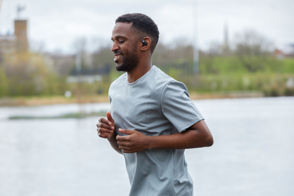 A smiling man running in a park using the earbuds