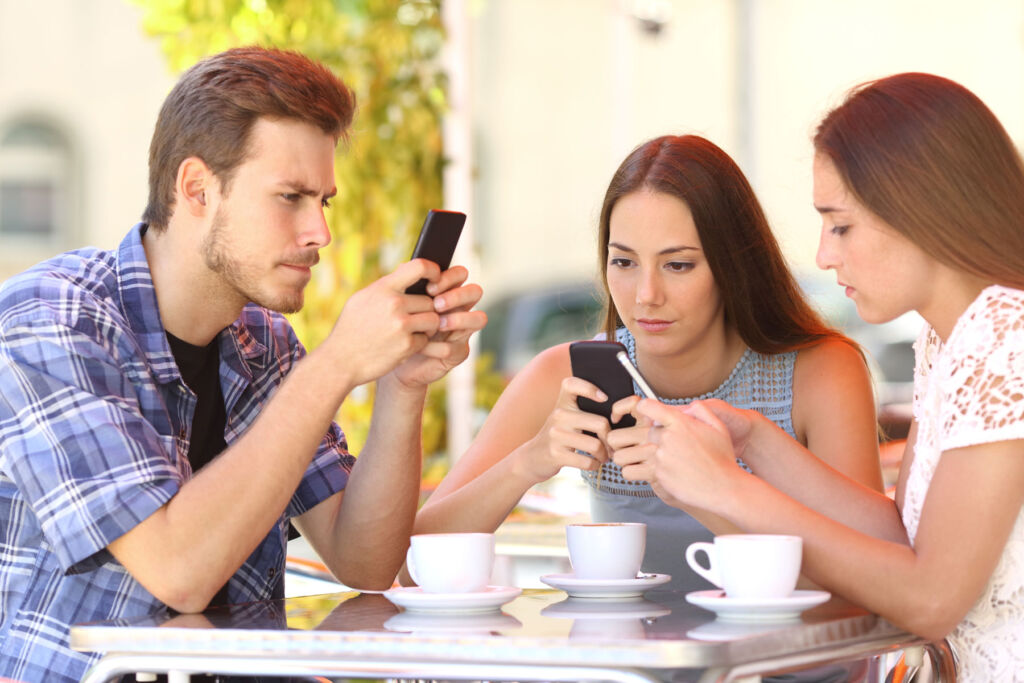 Three young people sat around the table, unable to look away from their phones