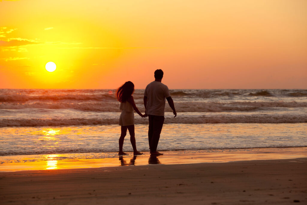 A couple holding hands while walking on the beach at sunset