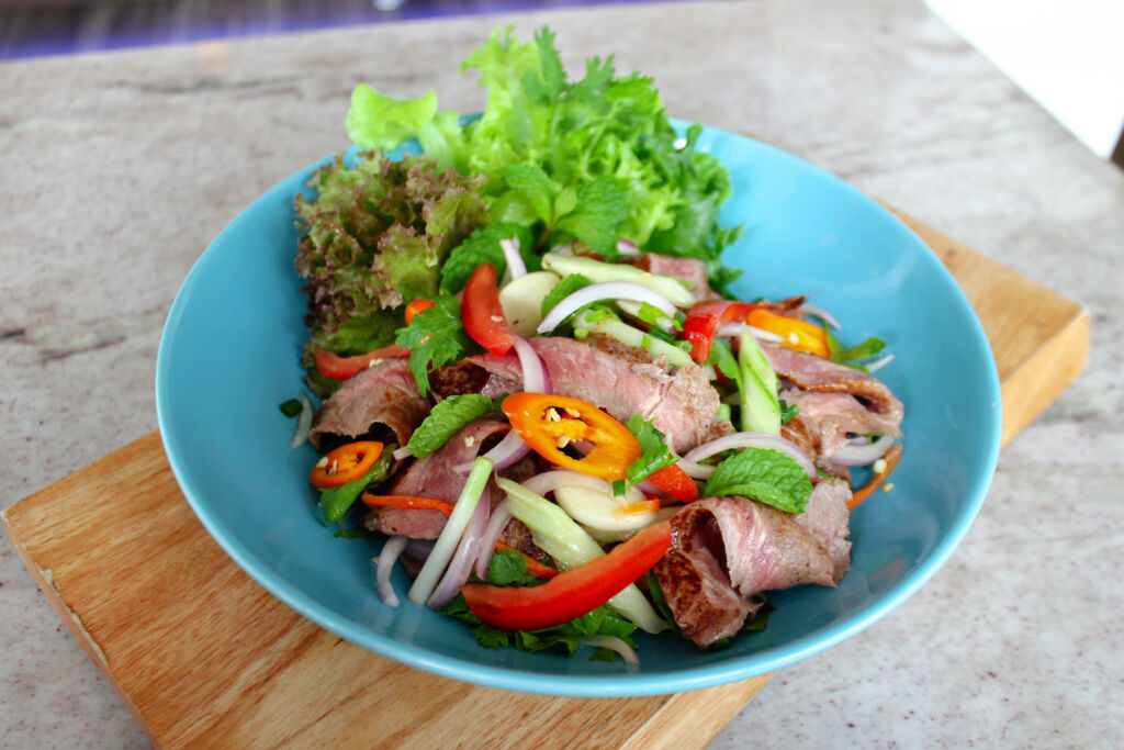 The Grilled Thai Beef Salad in a blue plate on a wooden board