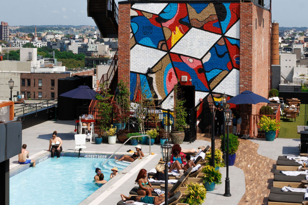 A photograph of people enjoying the rooftop swimming pool with the mural in the background
