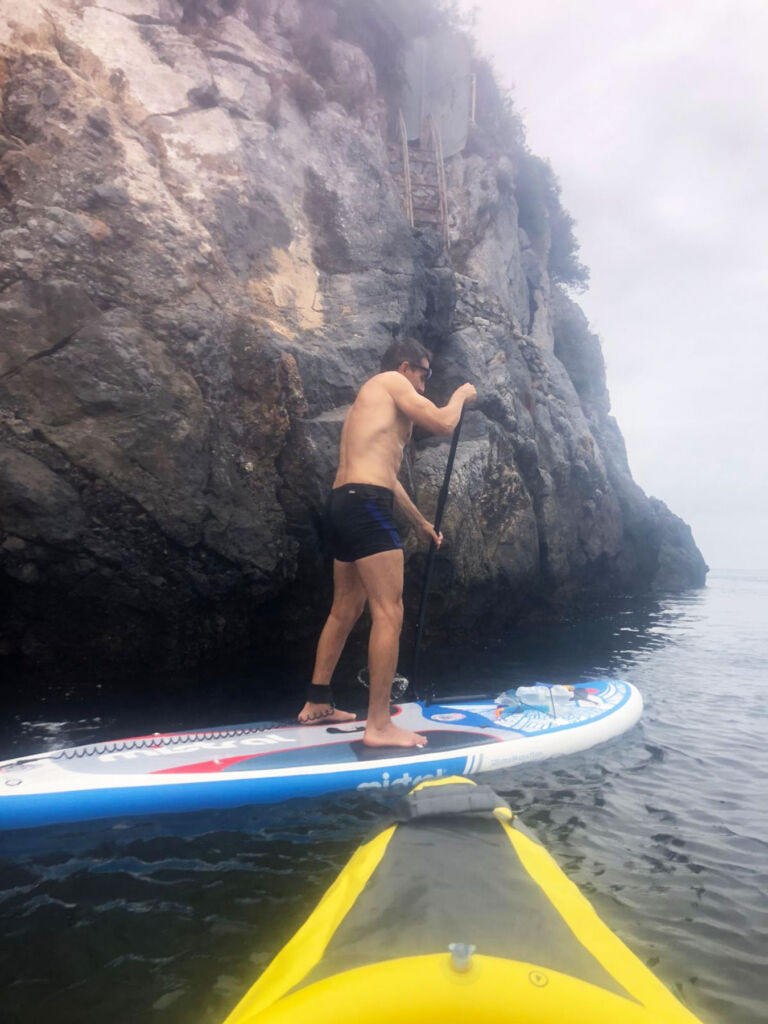 A man paddle boarding by a cliff face