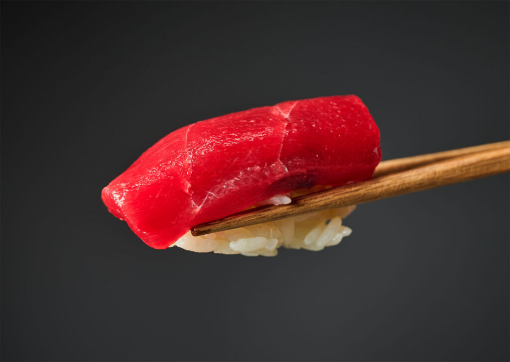 Fresh Tuna sushi on rice held between chopsticks