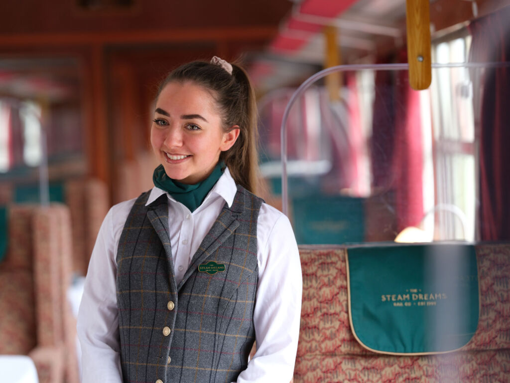 A young female of staff with a broad smile, eager to help guests on the train