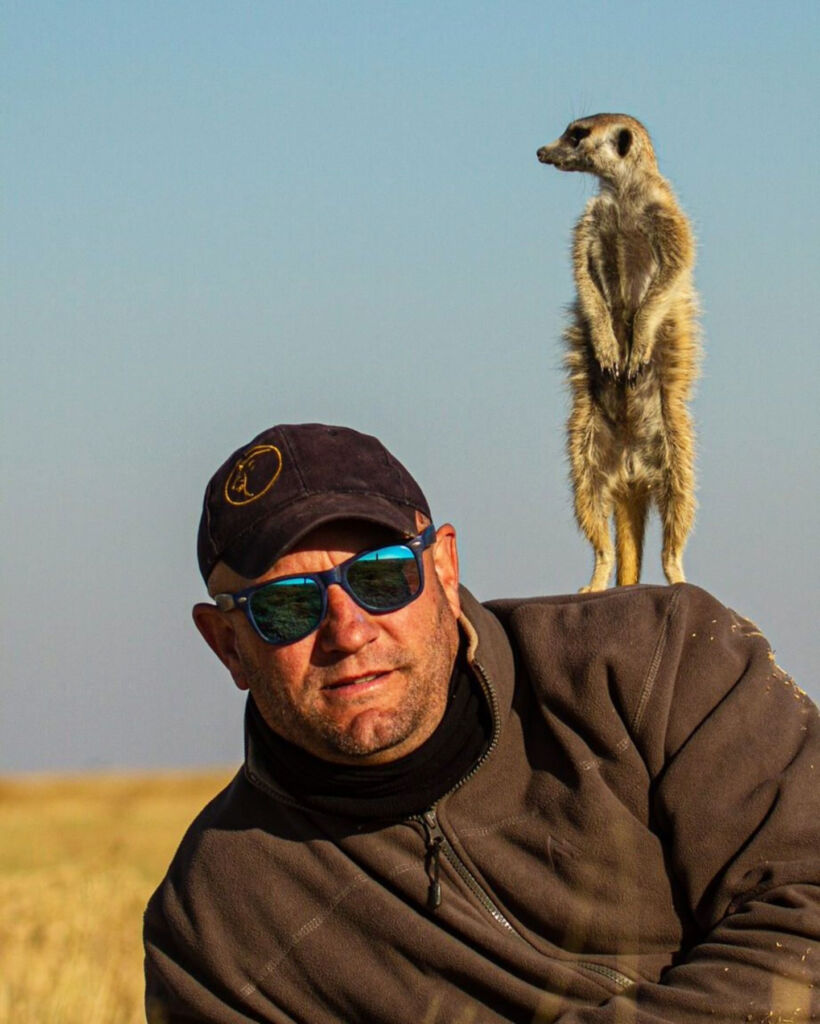 Shaun relaxing on the ground with a meerkat keeping watch standing on his shoulder