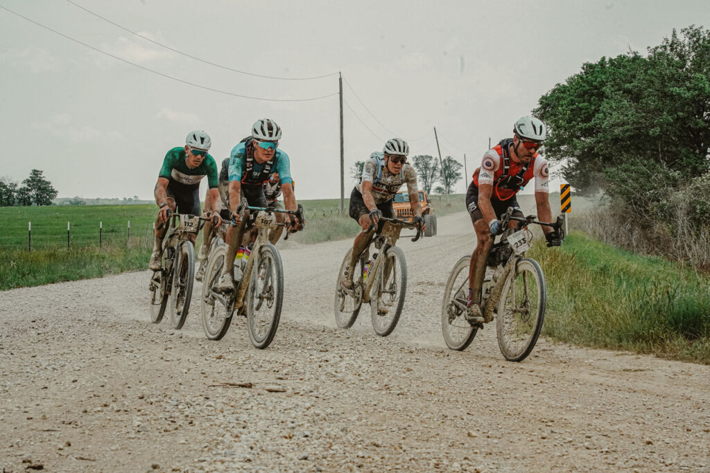 A small group of riders taking a bend at pace, kicking up the dust