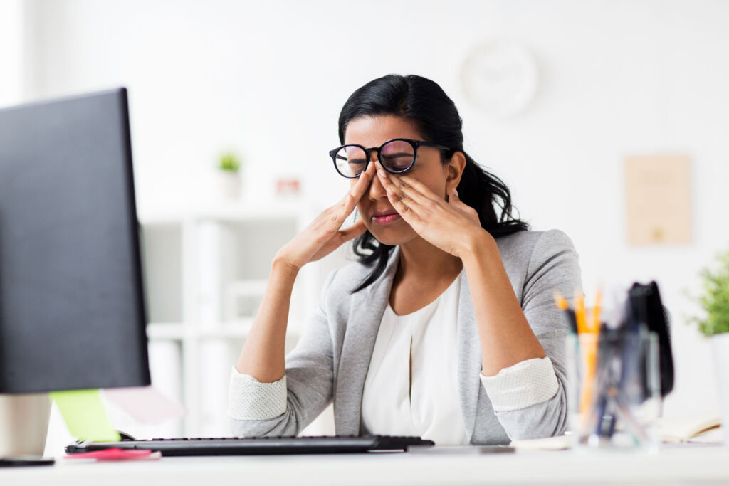 A woman rubbing her eyes in front of a computer screen