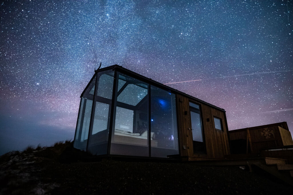 A photograph showing the exterior of the glass lodge under a starry sky at night