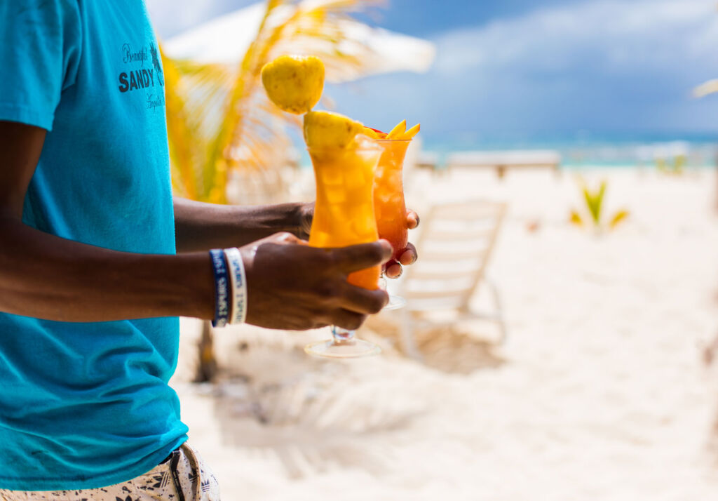 A man holding a cocktail as he walks across the beach