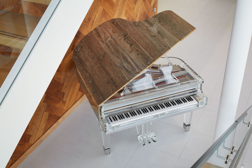 An elevated view of a piano with a see-thru exterior and wooden lid