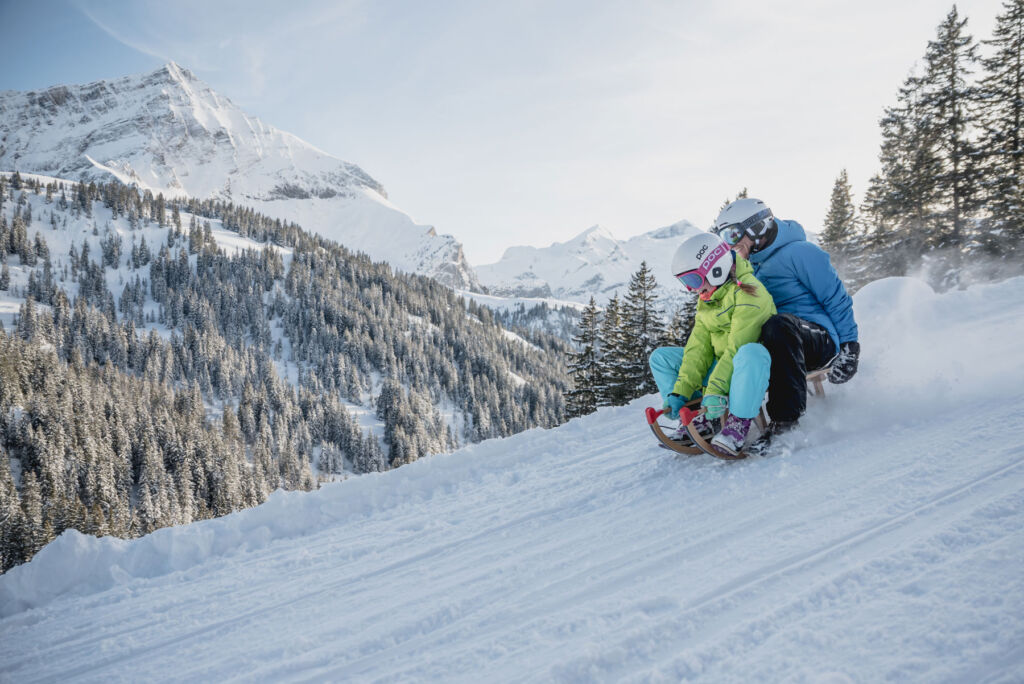 A parent and child sledding down a snowy slope