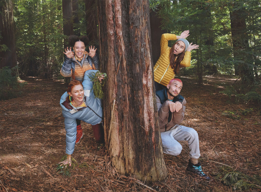 Four young people jumping out from behind a tree wearing the jackets in a variety of colours