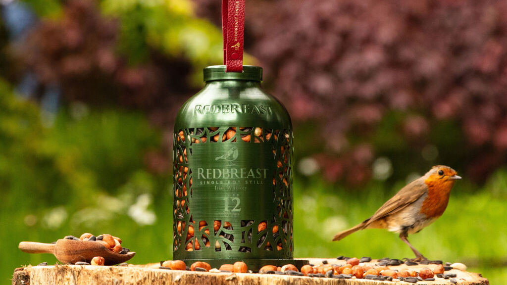 The green bird feeder in a garden being inspected by a robin
