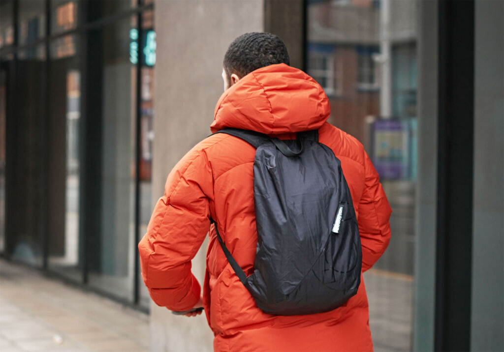 A man wearing an orange jacket wearing the backpack while walking along a high street