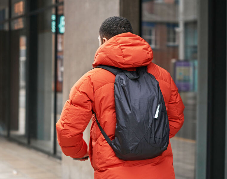 A man wearing an orange jacket wearing the backpack while walking along a high street