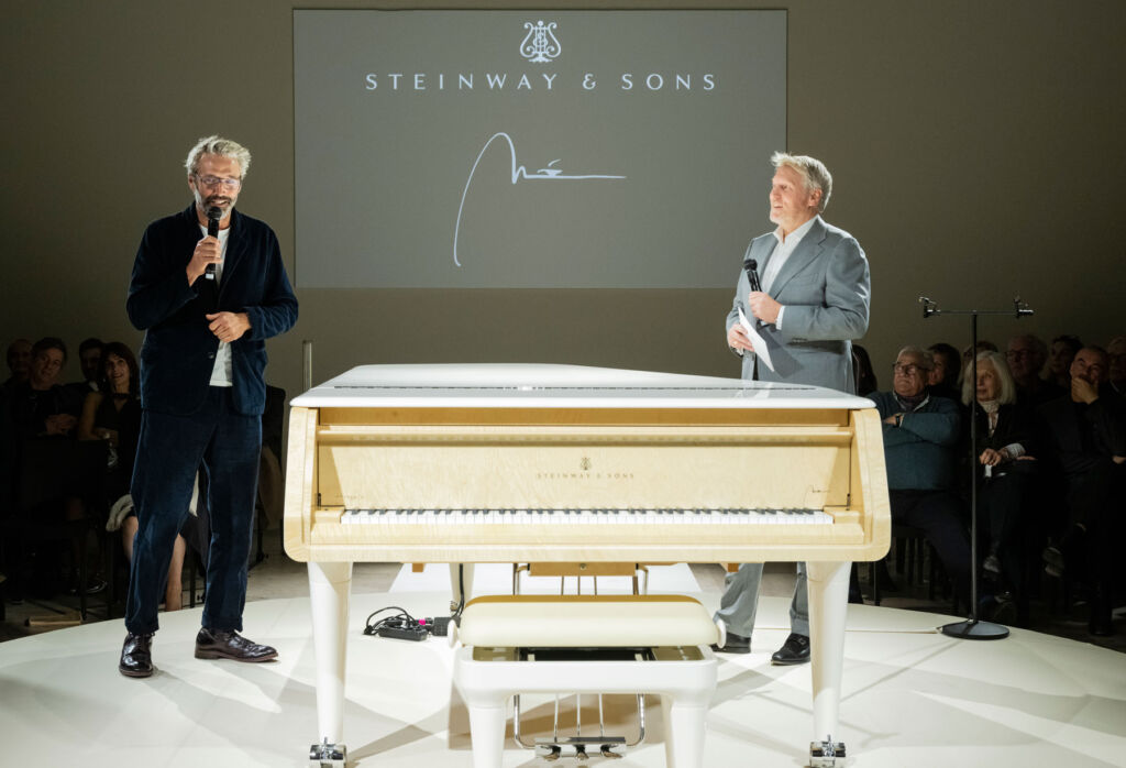 Guido talking to the audience by a white version of the piano