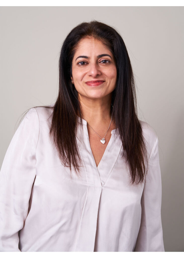 A smiling Anara wearing a long shirt