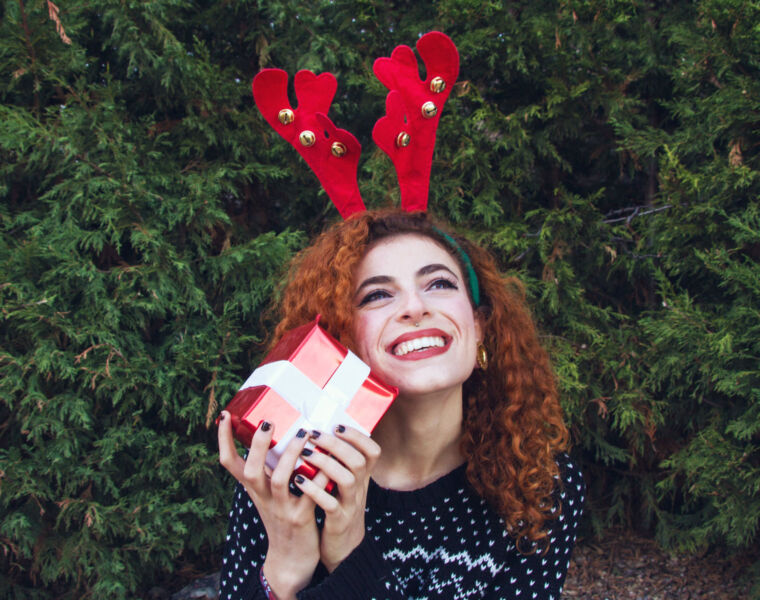 A woman with reindeer antlers on her head holding a Christmas present in her hands