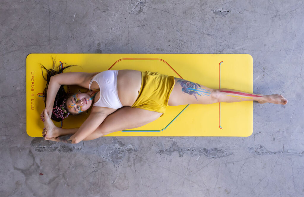 A top down view of a woman doing a yoga pose on a yellow, customised mat