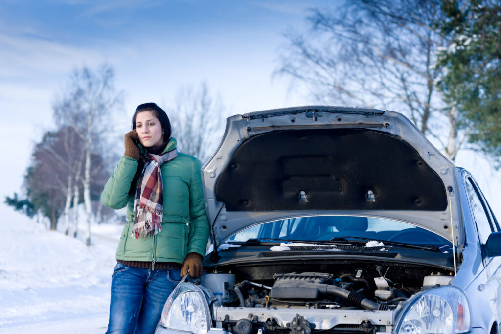A woman calling for assistance by her car in a snowy environment, which has a flat battery
