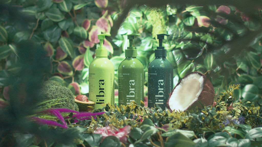 Three of the products in a setting filled with greenery, next to half a coconut