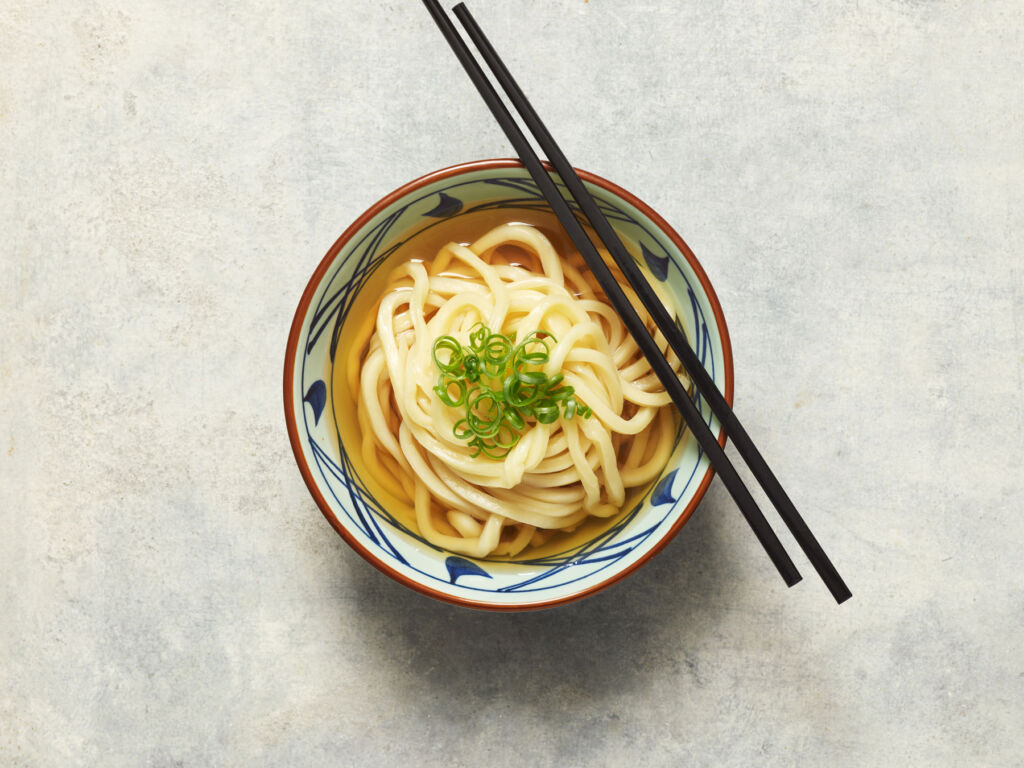 A bowl of noodles with chopsticks resting on top of the bowl
