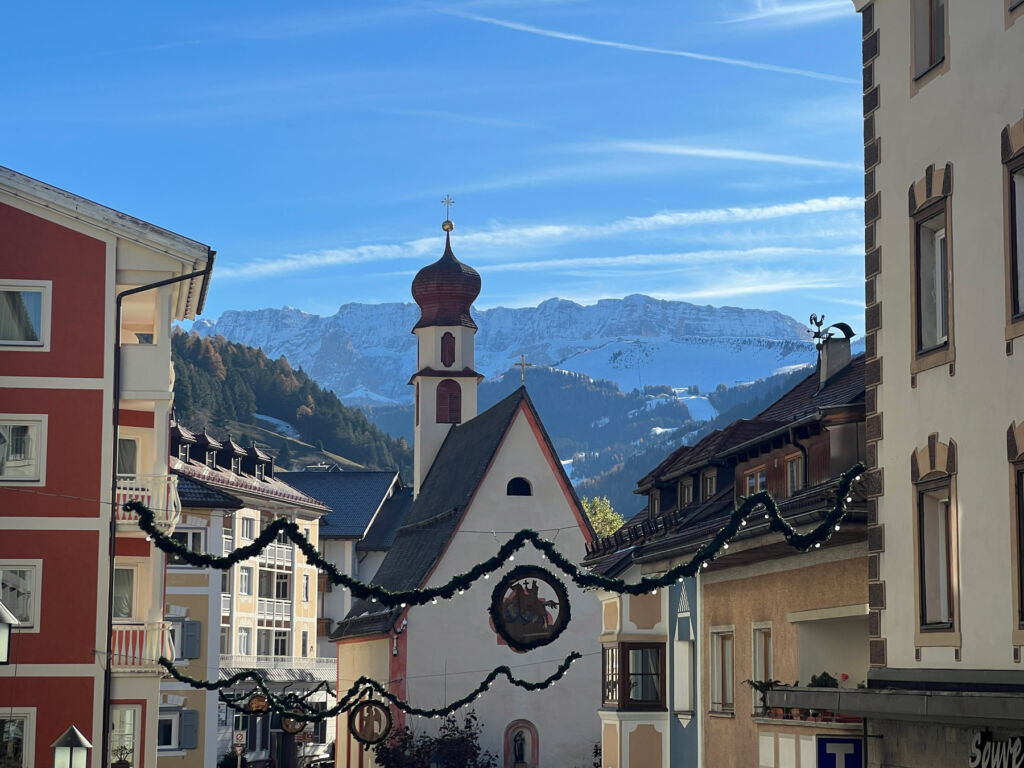 A photograph of the buildings in Ortisei Town, with the snow capped mountains in the distance