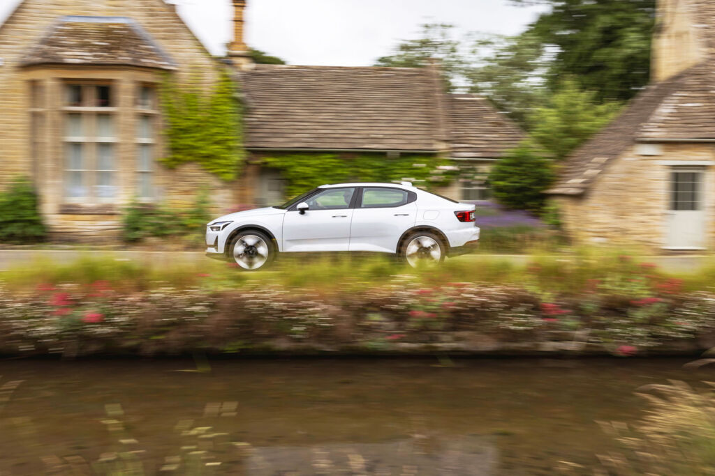 A side view photograph of the car being driven through an English village next to a river
