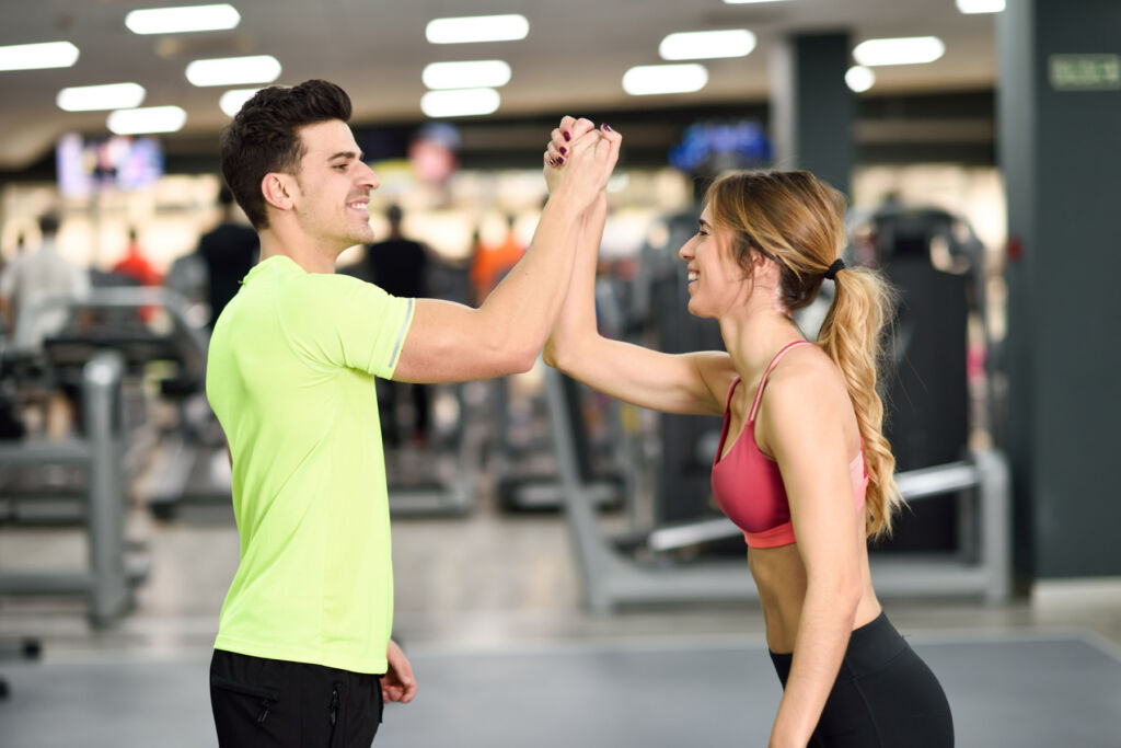 A man and a woman high-fiving each other after a workout session in the gym