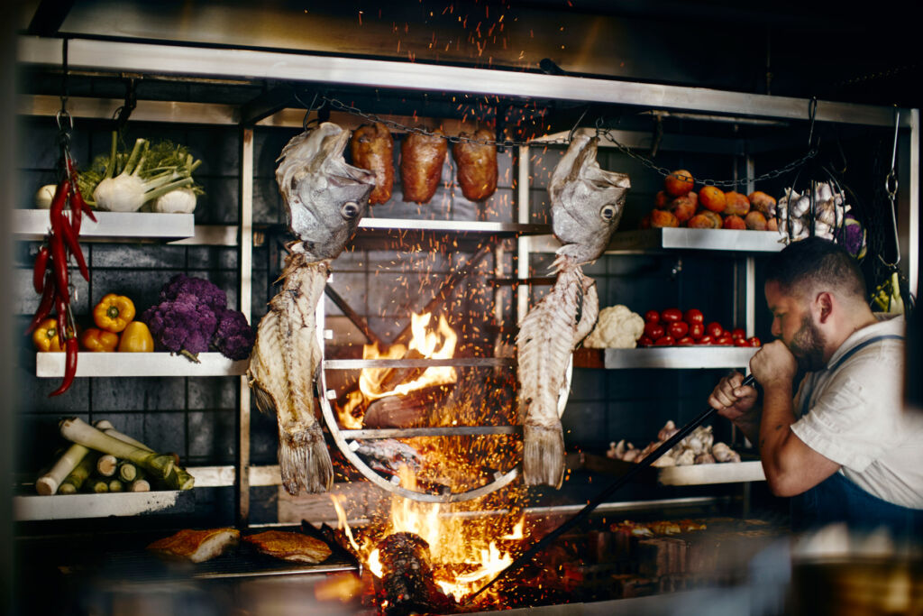 A member of the kitchen team blowing air into the fire, which is cooking the fish