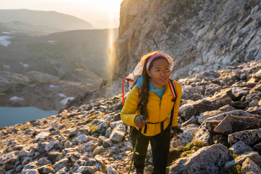 A young woman hiking up a rocky hill using poles