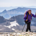 A woman who has reached the top of a mountain using the walking poles