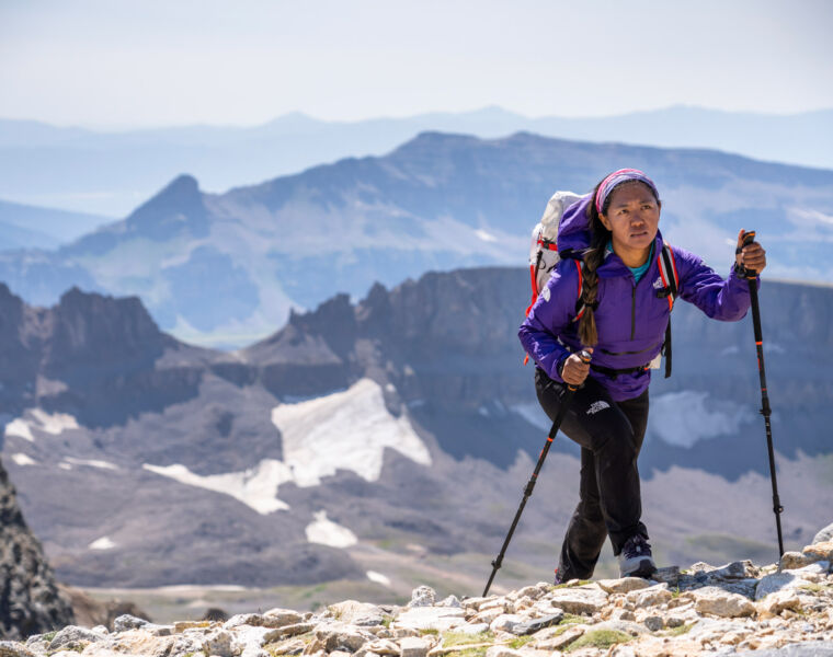 A woman who has reached the top of a mountain using the walking poles