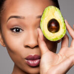 A woman holding a avocado to her face