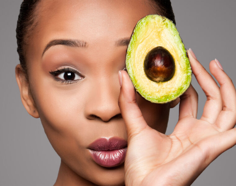 A woman holding a avocado to her face