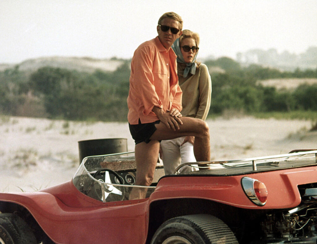 The actor Steve McQueen standing up in the Dune Buggy with his co-star