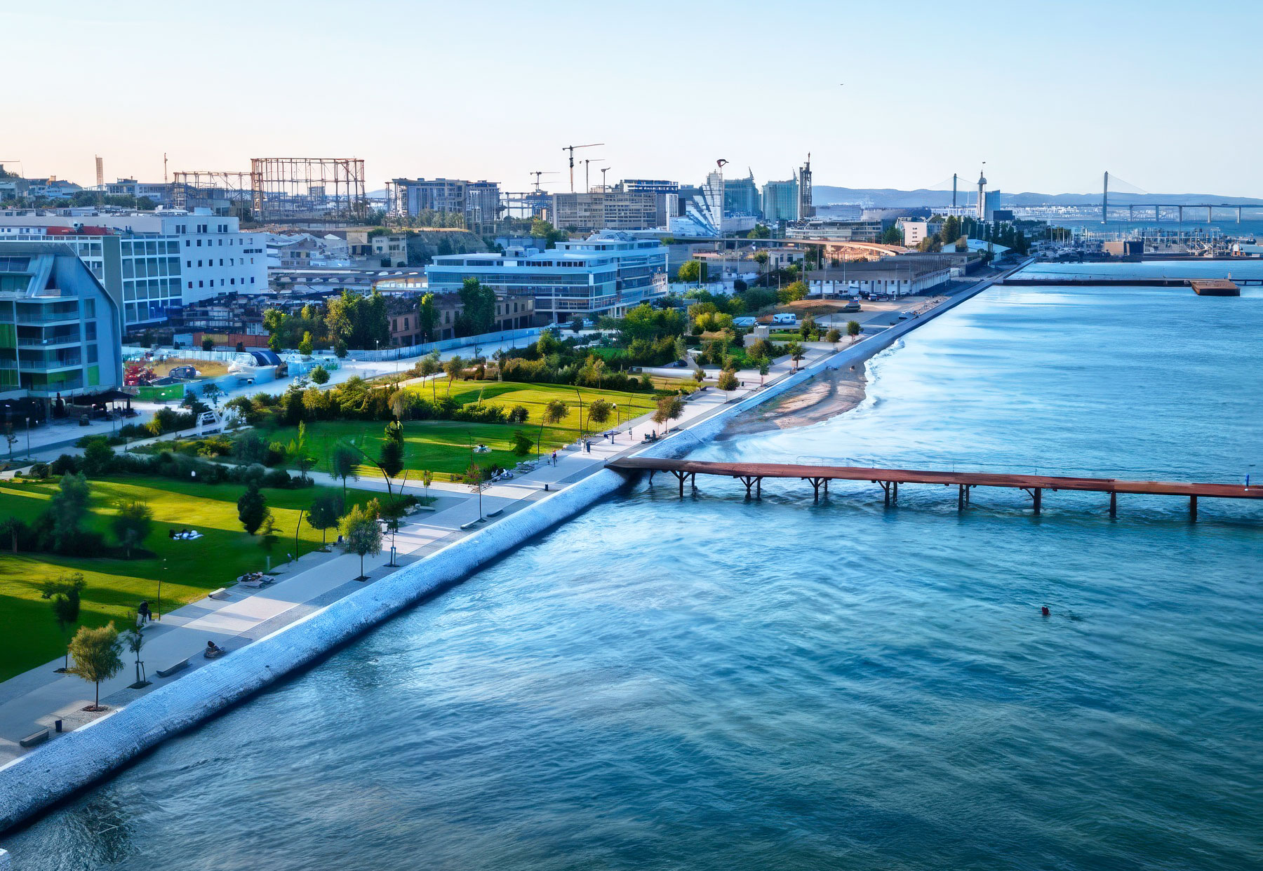 Scenic view of Marvila and Beato's revitalized riverfront area along the Tagus River, showing converted warehouses, street art, and modern developments with Lisbon's 25 de Abril Bridge in background