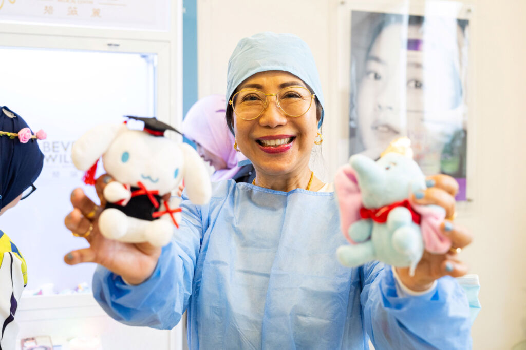 A smiling nurse holding up two small furry toys to the camera