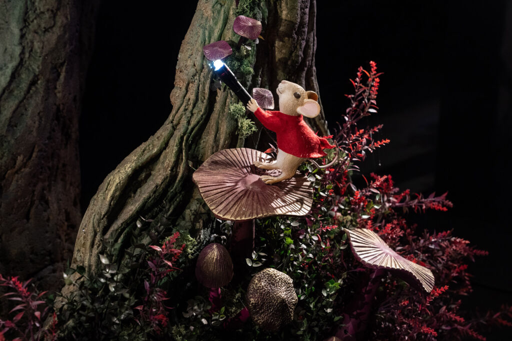 A mouse wearing a red jacket holding a lit torch by a tree