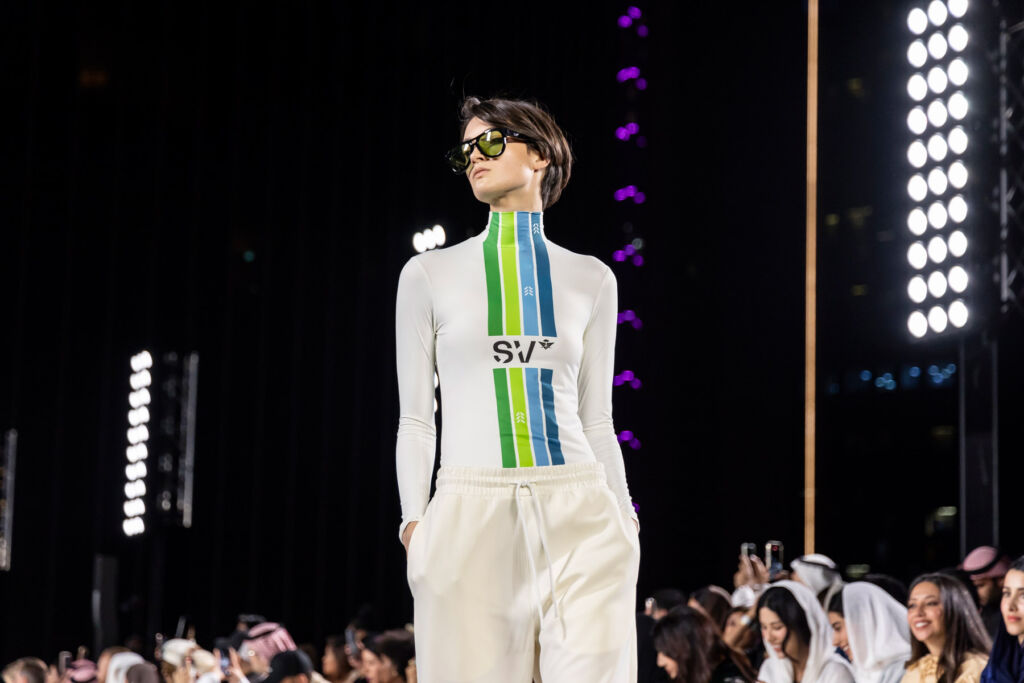 A female model wearing a tight-fitting white top with green and blue stripes