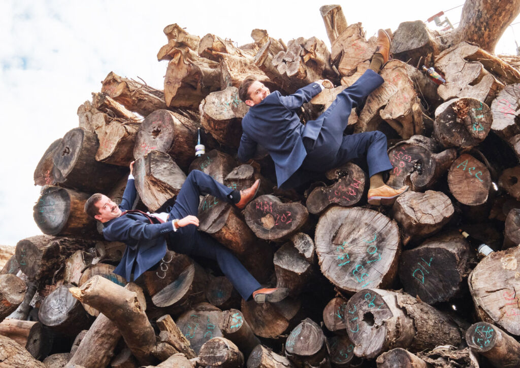 Two suited members of the team climbing a wood pile